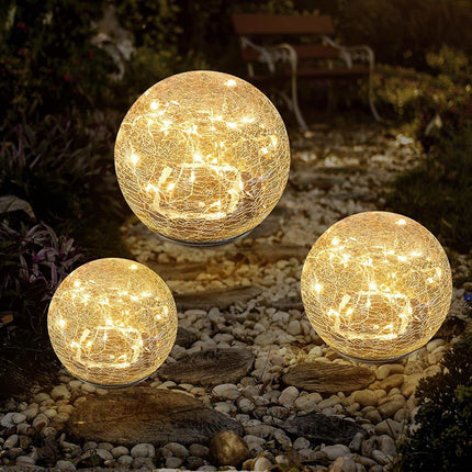 Solar Crackle Ball Light glowing warmly in garden at night with solar panel on top