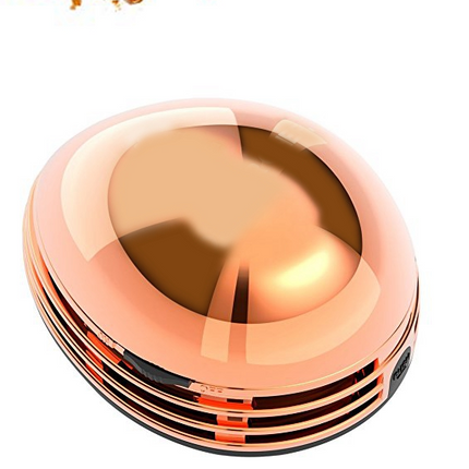 Portable mini desktop vacuum cleaner in gold color on a desk cleaning crumbs and dust